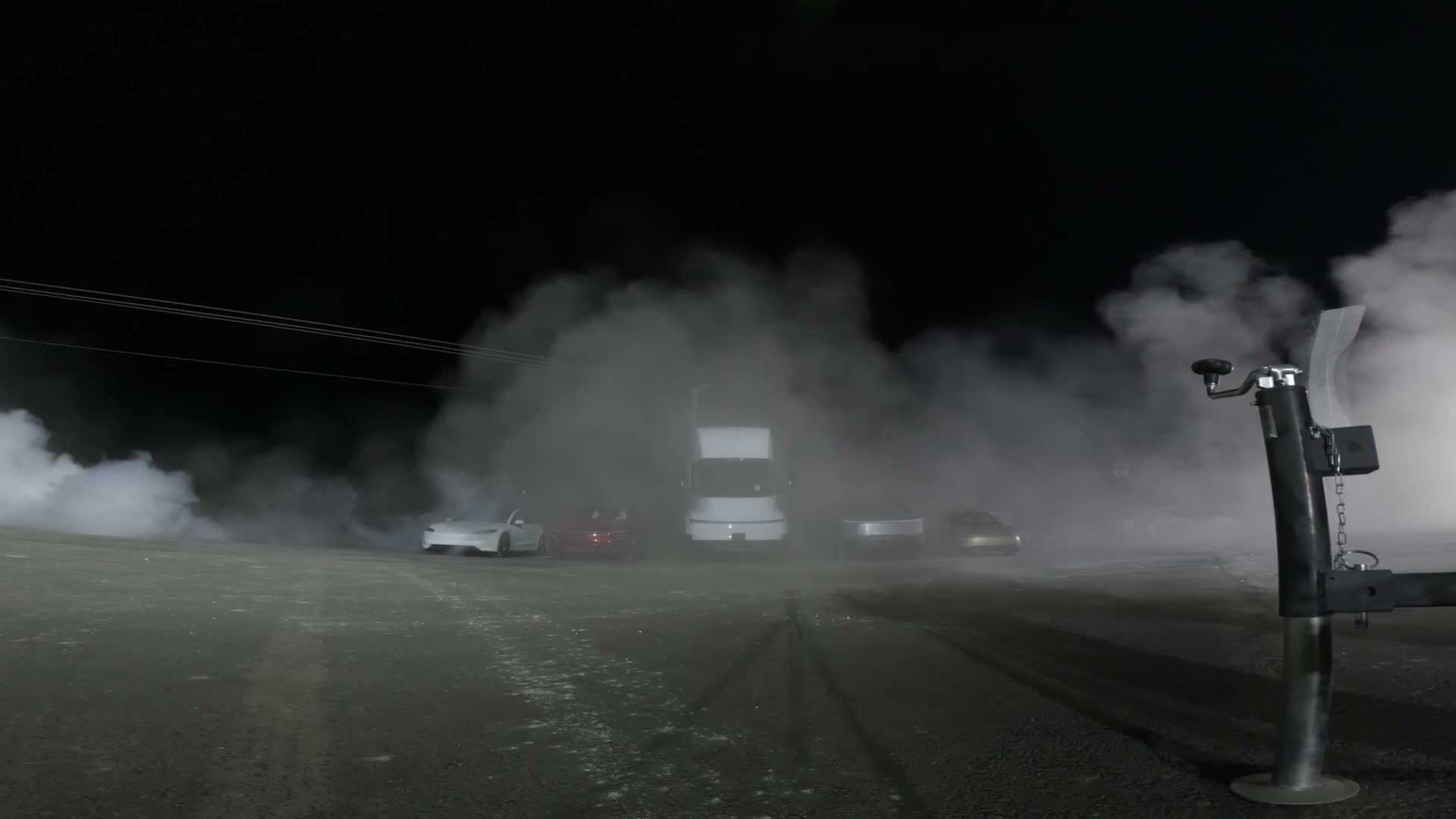Four Teslas in a line under blue vapor — the red Roadster, a white Tesla, the Semi and the Cybertruck